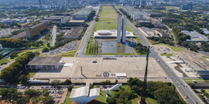 Fotografia colorida aérea que mostra a Praça dos Três Poderes em primeiro plano e a Esplanada dos Ministérios ao fundo, em Brasília, com destaque para o Congresso Nacional, que ocupa o centro da foto.